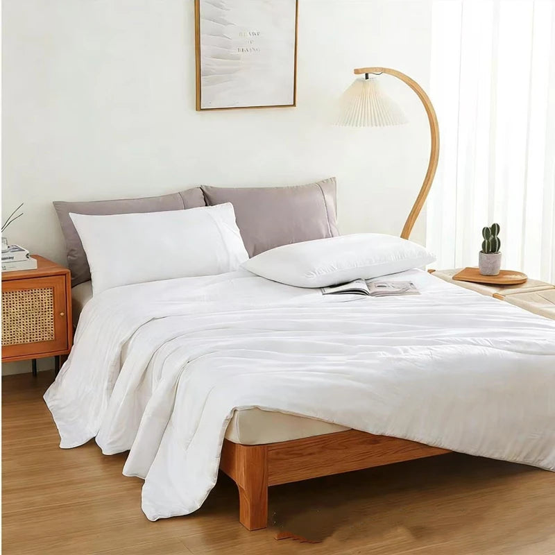 Ivory White bamboo fibre cooling quilt laid over a styled minimalist bedroom with a wooden bed frame, rattan bedside table and a curved bamboo floor lamp, creating a calm and airy summer sleep setting