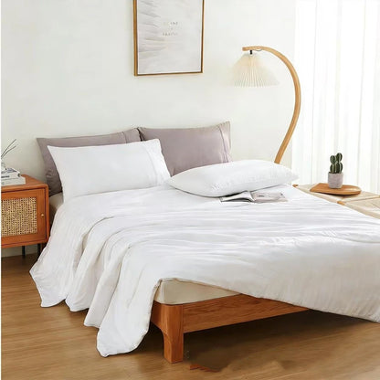 Ivory White bamboo fibre cooling quilt laid over a styled minimalist bedroom with a wooden bed frame, rattan bedside table and a curved bamboo floor lamp, creating a calm and airy summer sleep setting