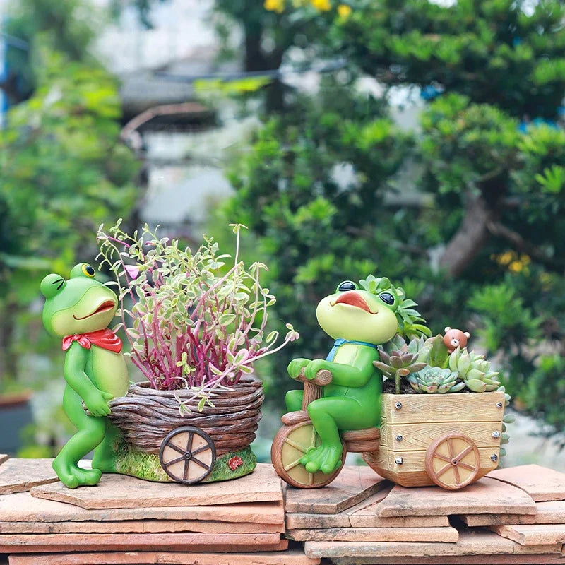 "Frog Tale" resin frog planters — Basket Hauler and Cycle Cargo styled with succulents on a terracotta tile surface with garden greenery background