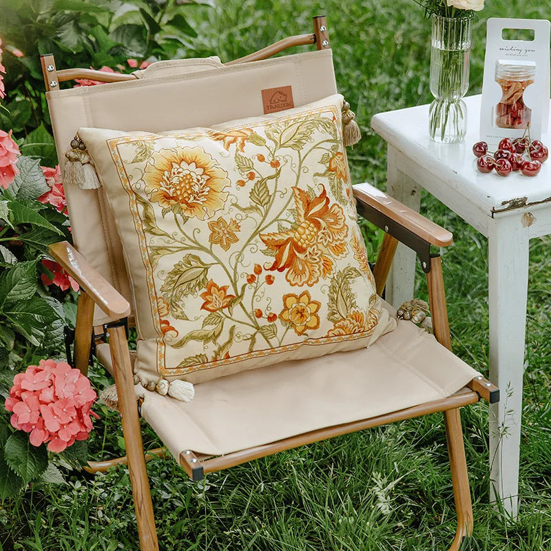 "Wild Harvest" floral embroidered cushion cover styled on a wooden garden chair surrounded by pink hydrangeas, amber and gold botanical motifs on ivory velvet — CL House Cushions collection