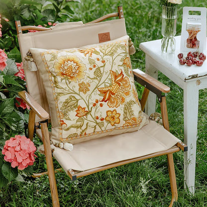 "Wild Harvest" floral embroidered cushion cover styled on a wooden garden chair surrounded by pink hydrangeas, amber and gold botanical motifs on ivory velvet — CL House Cushions collection