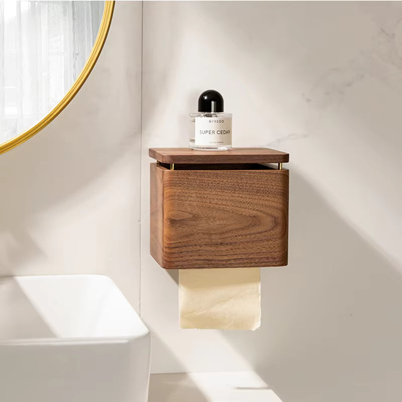 Walnut wood tissue holder mounted on bathroom wall with paper roll dispensing below and perfume bottle on top shelf, gold mirror in background — japandi bathroom styling