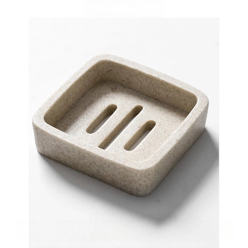 Square stone-texture resin soap dish in warm sand beige with three raised drainage slots, top angle view, white background