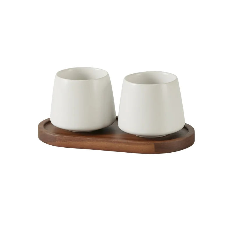 Two cone-shaped matte white ceramic cups on oval acacia wood tray, clean white finish, bathroom toothbrush holder set, white background