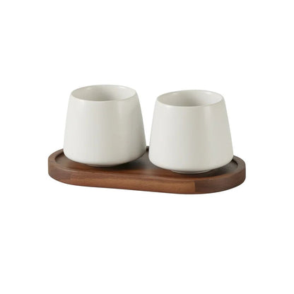 Two cone-shaped matte white ceramic cups on oval acacia wood tray, clean white finish, bathroom toothbrush holder set, white background