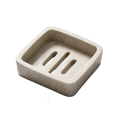 Square stone-texture resin soap dish in warm sand beige with three raised drainage slots, top angle view, white background