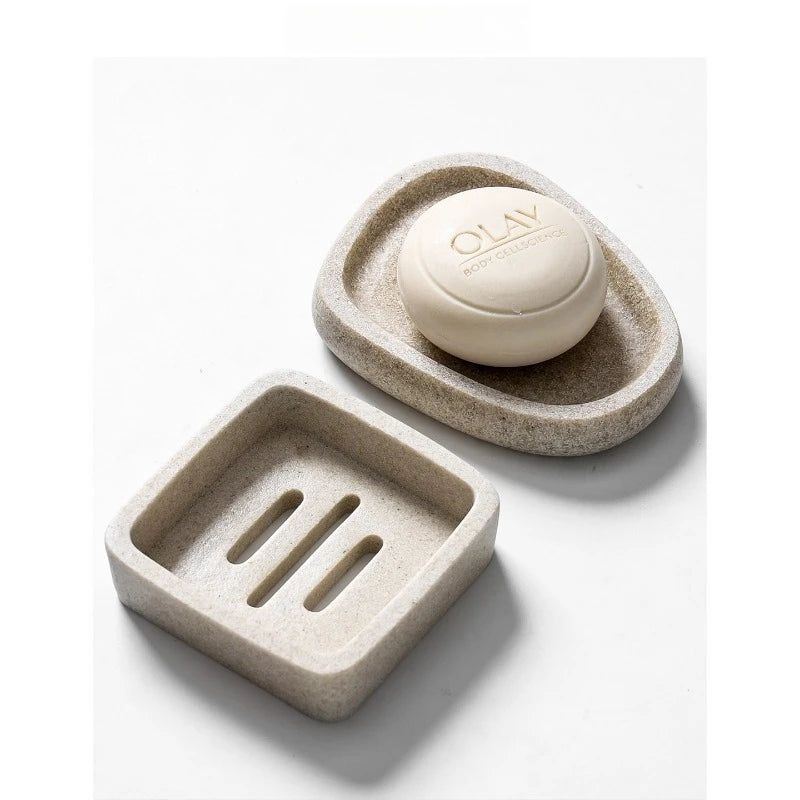Pebble resin soap dish holding a white soap bar alongside square soap dish with drainage slots, sand beige stone-texture, bathroom vanity styling