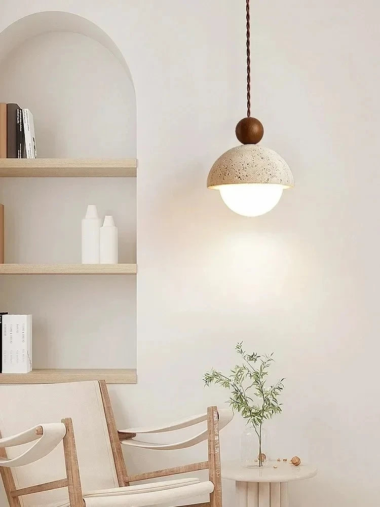 Stone & Orb travertine pendant light with walnut wood bead glowing warm light in a japandi living room styled with wooden shelves, linen chairs and a small green plant on a side table
