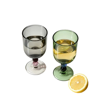 "Chromatic Orb" glass goblets in smoke grey and forest green filled with white wine, on a white background with a halved lemon