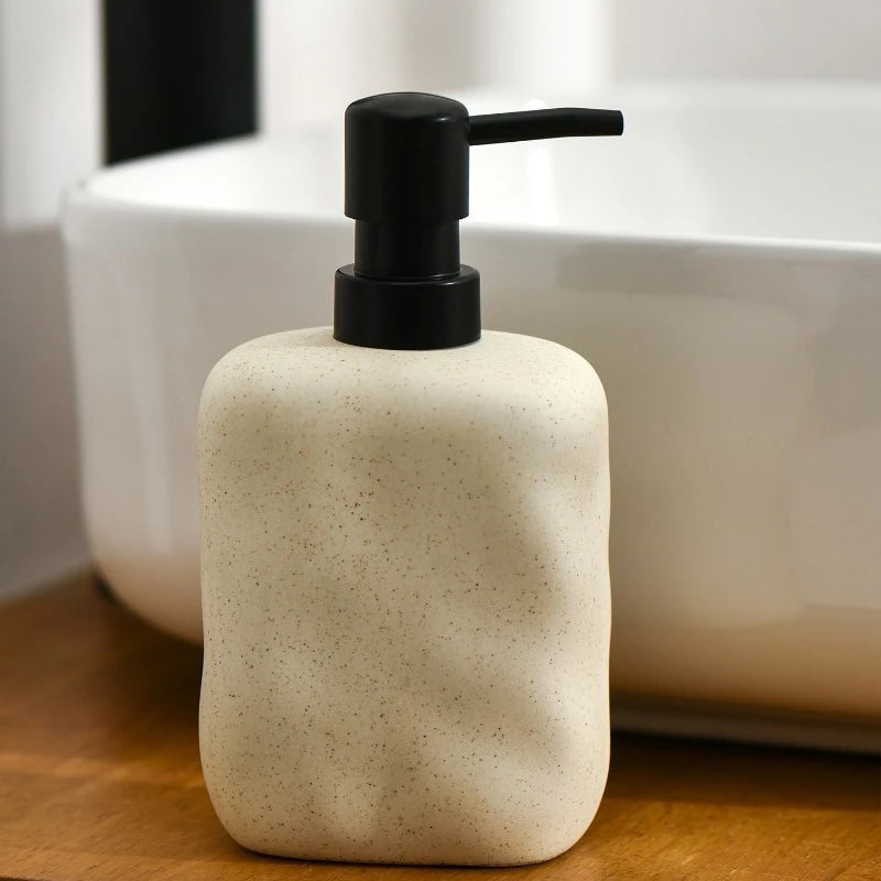  Sand Form ceramic soap dispenser with matte black pump on wooden vanity shelf next to white ceramic vessel sink, bathroom setting with mirror reflection in background