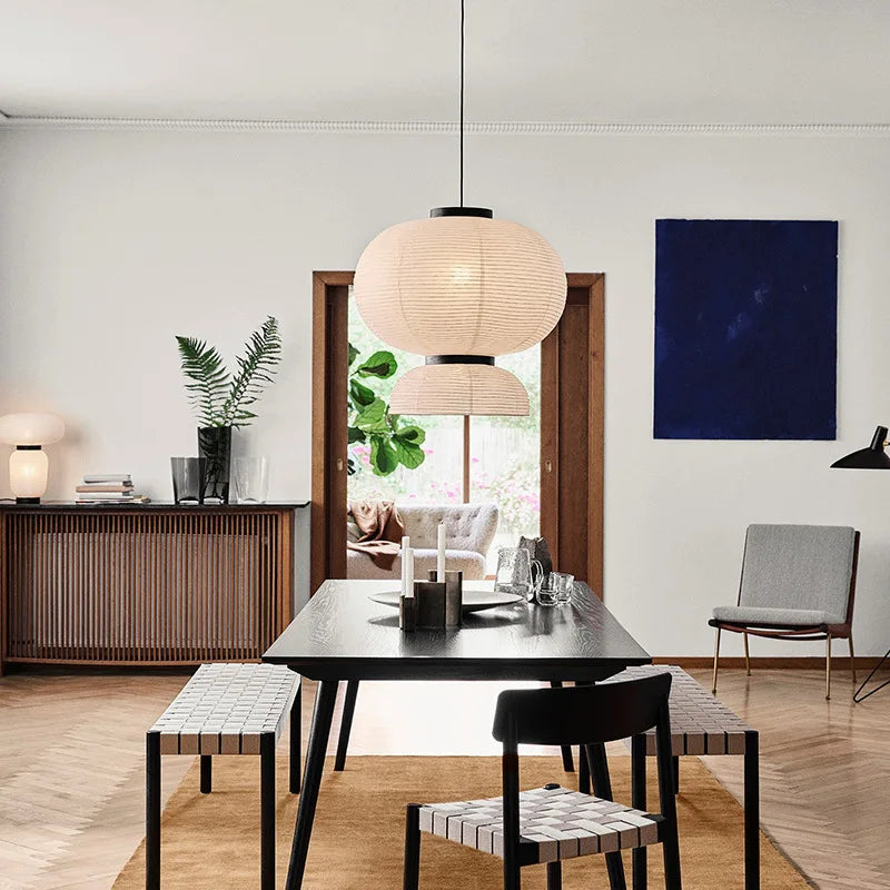 Rice & Ripple paper pendant light hanging above a black dining table in a bright Scandinavian dining room with wooden floors, indoor plants and a blue artwork on the wall
