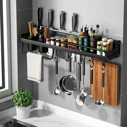 Matte black wall-mounted kitchen organiser shelf fully loaded in a grey tiled kitchen — knives in slots at top, spices and condiments on shelf, chopstick and utensil cups, 8 hooks with pots, ladles and spatulas hanging, chopping board and kitchen towel — lifestyle hero shot of the Black Rail Kitchen Organiser by CL House