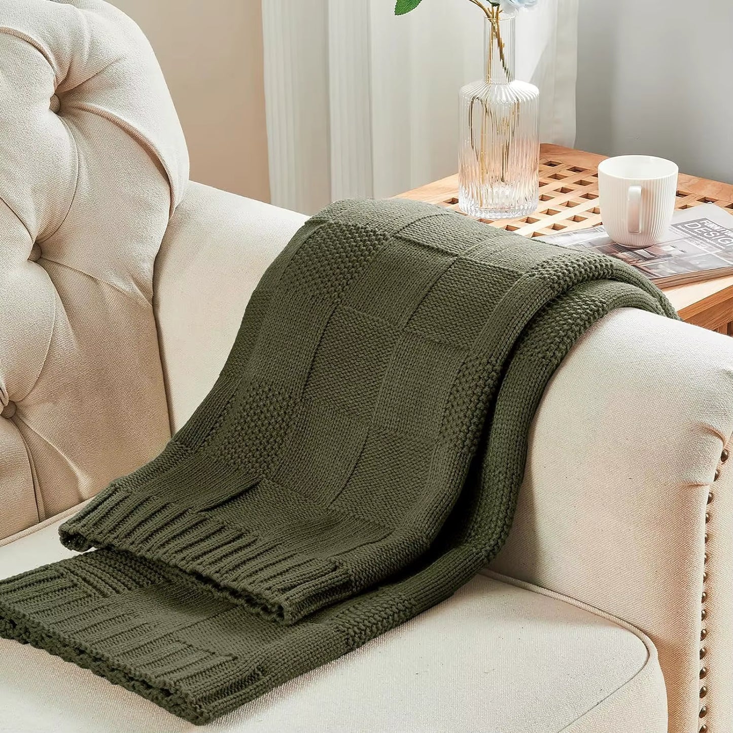 Forest Olive chunky patchwork knit throw blanket draped over a beige tufted sofa — mixed knit texture and fringe border detail with wooden side table