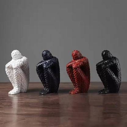 A group of seated mosaic resin figure sculptures in white, black and red finishes displayed on a wooden table.
