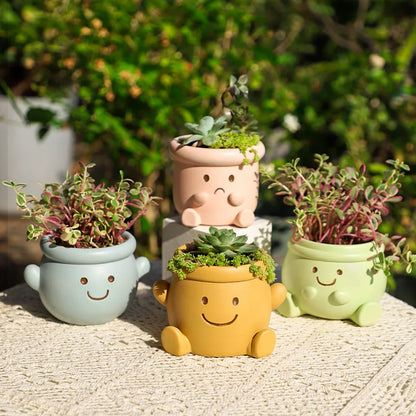 "Happy Pot" complete set of four smiley face resin succulent planters in sky blue, blush pink, mustard yellow and sage green, displayed outdoors with succulents in warm sunlight