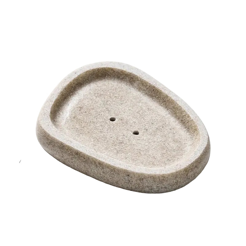 Oval pebble-shaped stone-texture resin soap dish in warm sand beige with two drainage holes, top angle view, white background