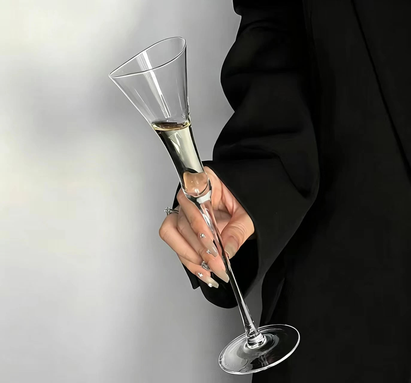 Hand holding a "Trumpet" crystal champagne flute filled with champagne, elegant trumpet-shaped silhouette — CL House Drinkware collection
