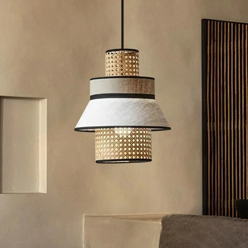  "Layer & Loom" tiered rattan and linen pendant light against a textured neutral wall with dark wood slat panel, japandi interior styling