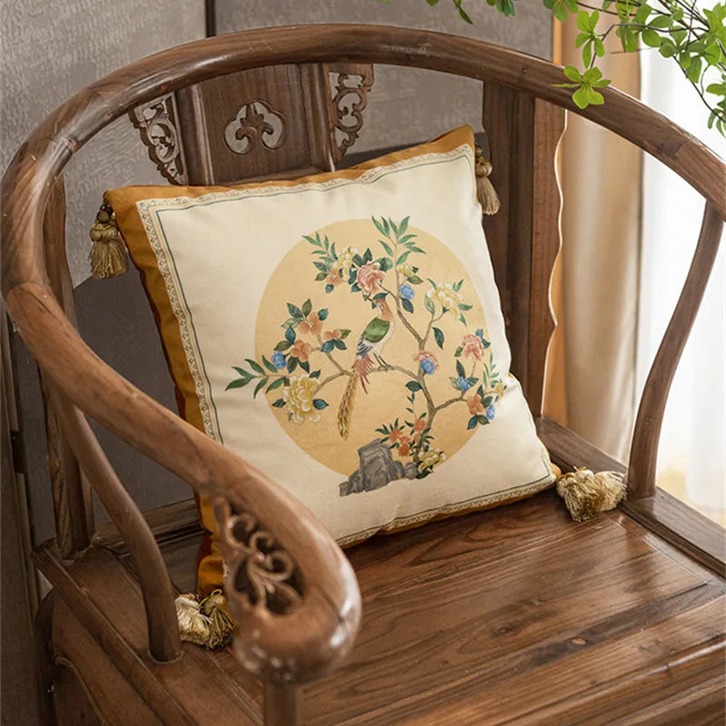 "Moon Blossom" chinoiserie velvet cushion cover styled on a carved dark wood armchair, circular bird and blossom motif on ivory ground with golden border and corner tassels — CL House Cushions collection