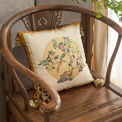 "Moon Blossom" chinoiserie velvet cushion cover styled on a carved dark wood armchair, circular bird and blossom motif on ivory ground with golden border and corner tassels — CL House Cushions collection