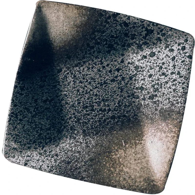 "Black Pearl" ceramic square dinner plate — close-up top view on white background showing reactive glaze detail with deep black, silver and warm bronze tones shifting across the surface — texture shot
