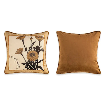 "Marguerite" botanical velvet cushion cover front and back view, warm caramel ground with bold black ink botanical illustration of zinnia flowers, cursive "marguerite" script in corner, plain caramel velvet reverse with coordinating piping — CL House Cushions collection
