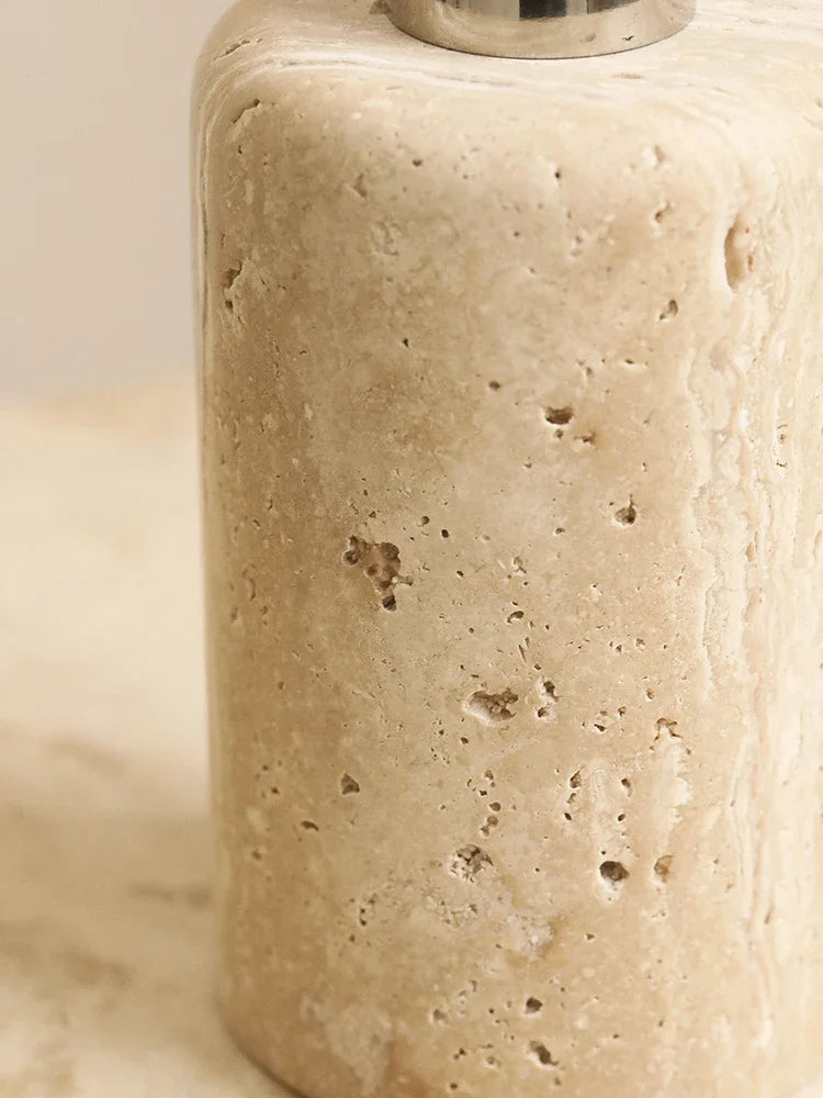 Close-up of natural travertine soap dispenser showing porous stone texture and fossil markings, warm beige tones — wabi-sabi bathroom detail