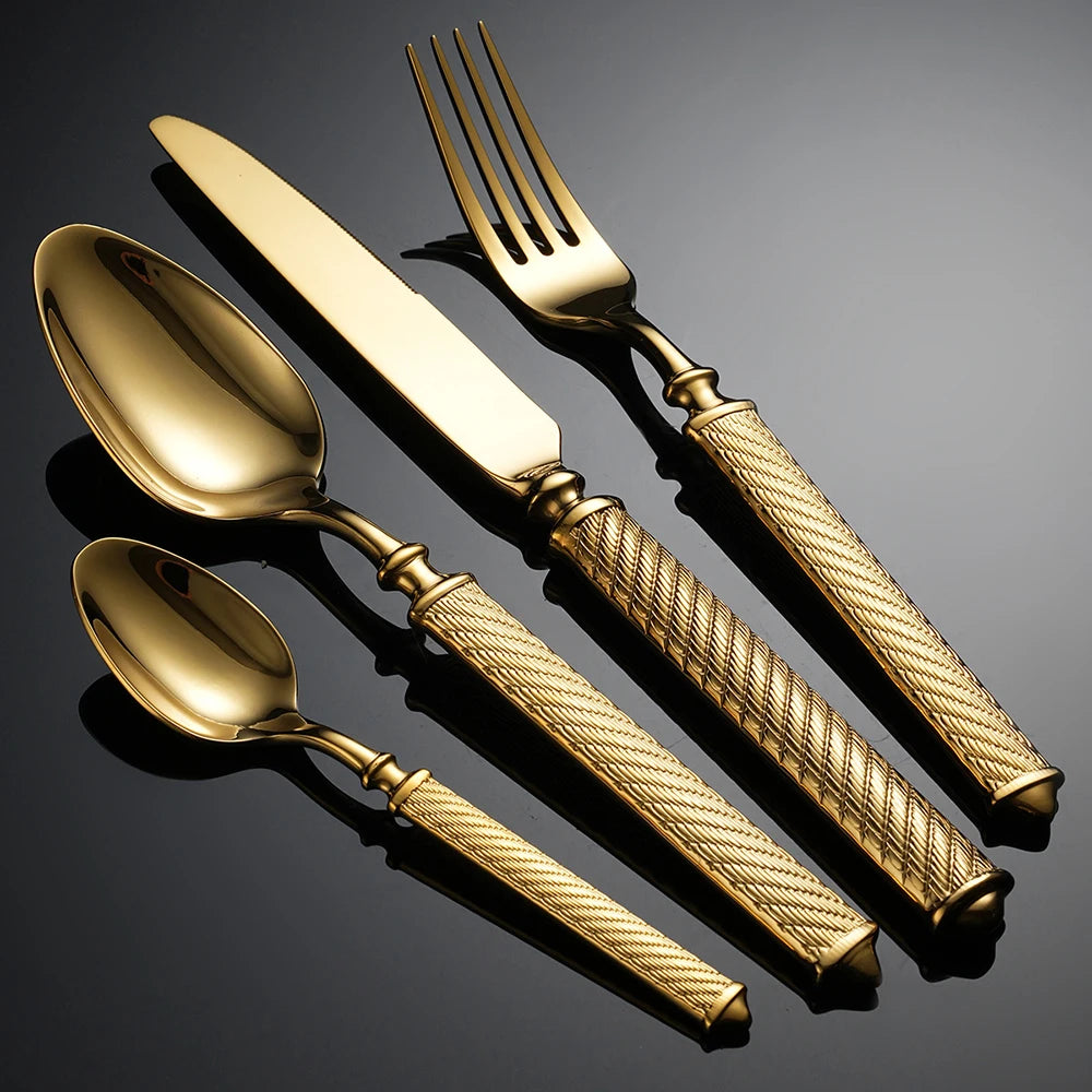  "Twisted Rope" gold stainless steel cutlery set of 4 pieces on a dark grey surface — dramatic lighting highlighting the hand-engraved twisted rope handle detail