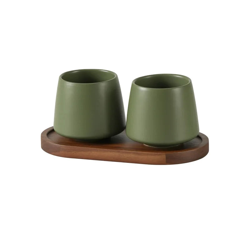 Two cone-shaped matte green ceramic cups on oval acacia wood tray, vintage green finish, bathroom toothbrush holder set, white background
