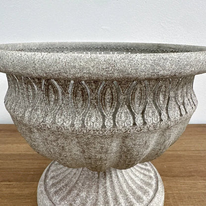 Roman Urn" ornate stone-texture garden urn planter, close-up detail of acanthus leaf relief pattern and textured rim, Stone Grey finish, shown on wooden surface