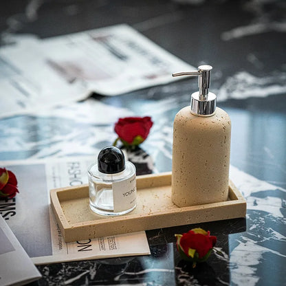 Rose Stone travertine soap dispenser on stone tray styled with Byredo perfume bottle and red roses scattered on dark marble surface
