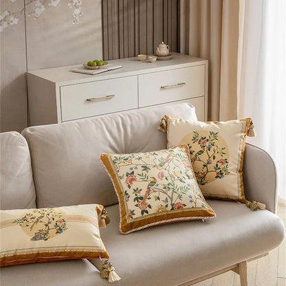 Three "Golden Garden" chinoiserie velvet cushion covers styled on a grey linen sofa in a neutral living room, square and lumbar sizes with exotic birds and peonies, gold braided border and corner tassels — CL House Cushions collection