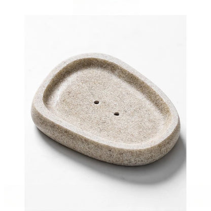 Oval pebble-shaped stone-texture resin soap dish in warm sand beige with two drainage holes, top angle view, white background