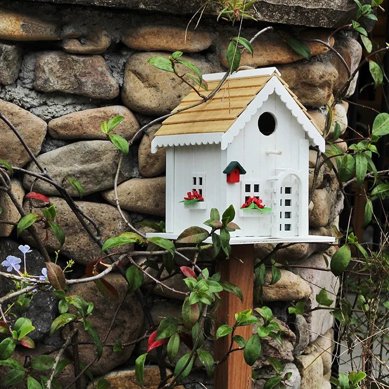 "Natural Wood House" wooden birdhouse on stake against rustic stone wall with climbing vines and wildflowers, cottage garden decoration outdoor