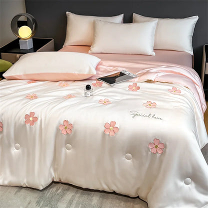 "Ice Bloom cooling summer quilt in Blossom Pink styled on a bed — ivory white with scattered embroidered pink daisy motifs and 'Special Love' script detail, blush pink reverse, lightweight summer bedding"