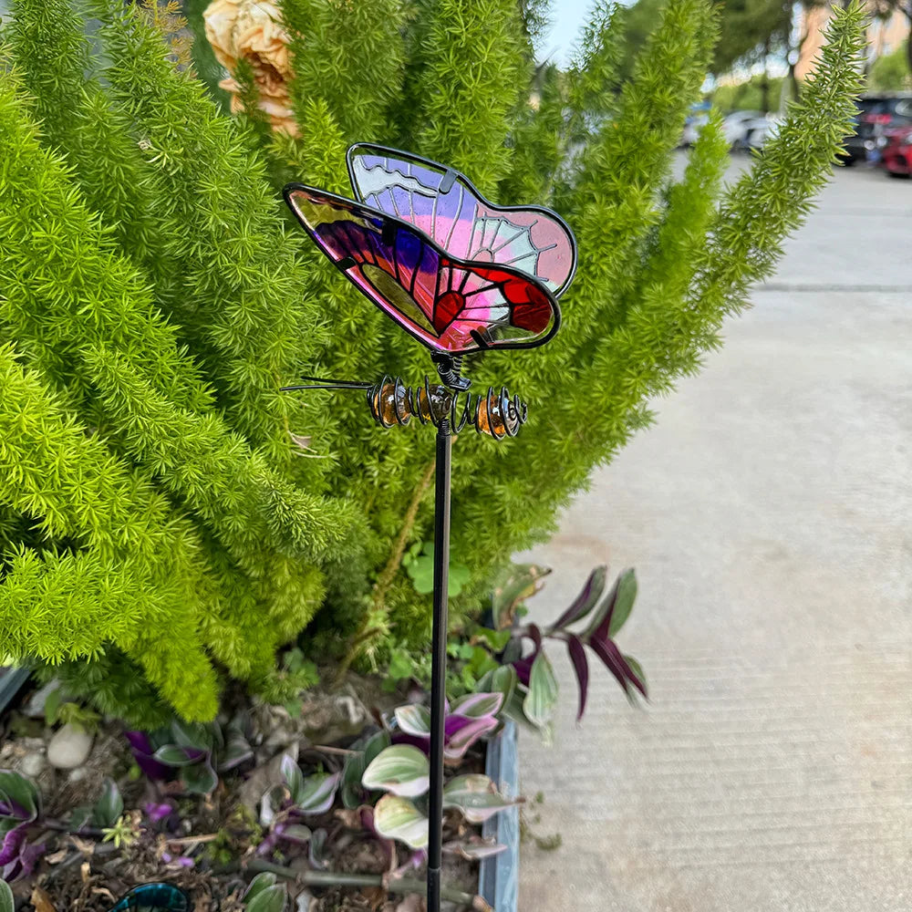 "Garden Wings" stained glass effect metal butterfly garden stake in pink-red-purple tones planted in an outdoor garden border with succulents and green foliage