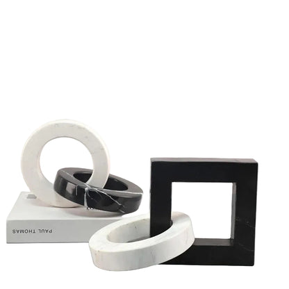 Round and square black and white interlocking marble sculptures displayed together on a neutral surface beside a book.