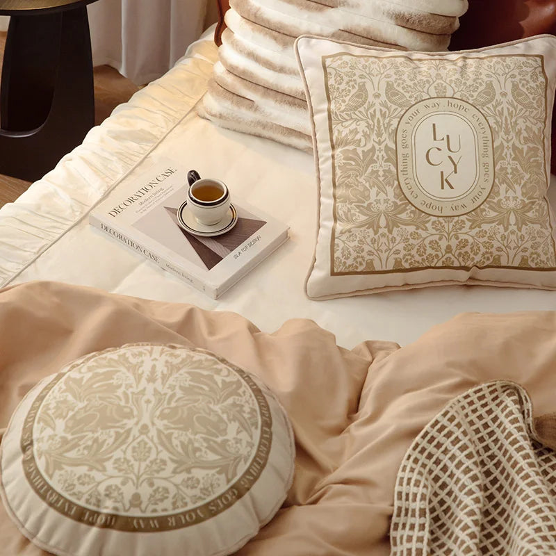 "Lucky Bloom" square and "Dark Forest" round botanical velvet cushion covers styled together on a neutral bedroom bed, warm beige and cream tones with golden floral motifs — CL House Cushions collection