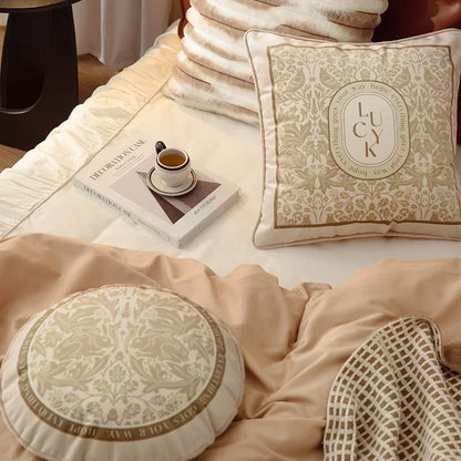 "Lucky Bloom" square and "Dark Forest" round botanical velvet cushion covers styled together on a neutral bedroom bed, warm beige and cream tones with golden floral motifs — CL House Cushions collection