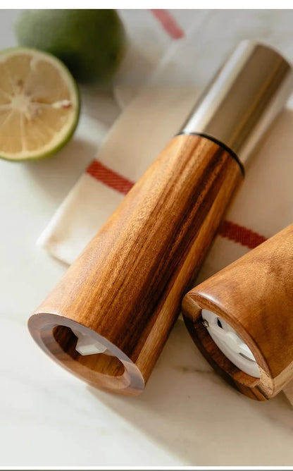 Acacia Twist salt and pepper mill set lying on a white marble surface showing the ceramic grinding mechanism base, styled with fresh limes