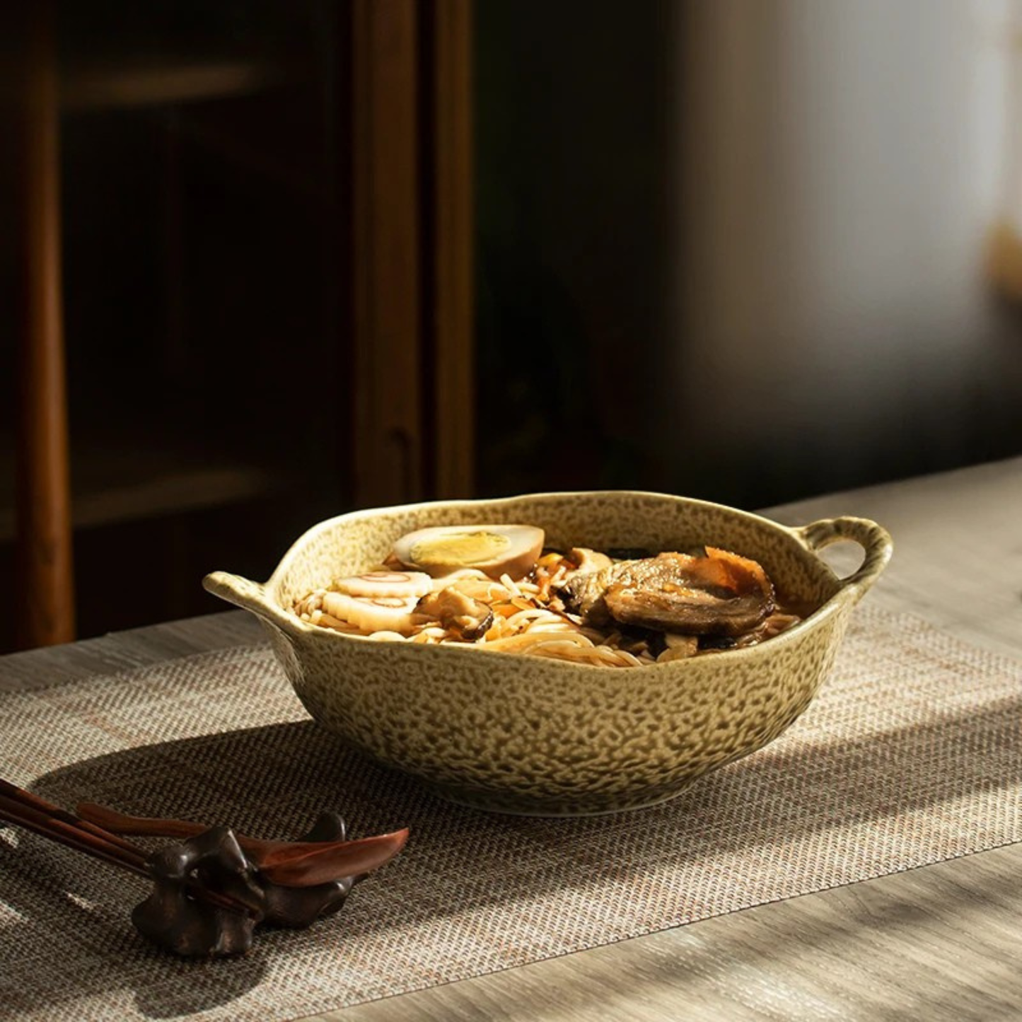 "Wabi Crest" stoneware serving bowl in stone cream filled with ramen noodles and toppings — lifestyle shot on linen table runner with wooden chopsticks and spoon in warm natural light