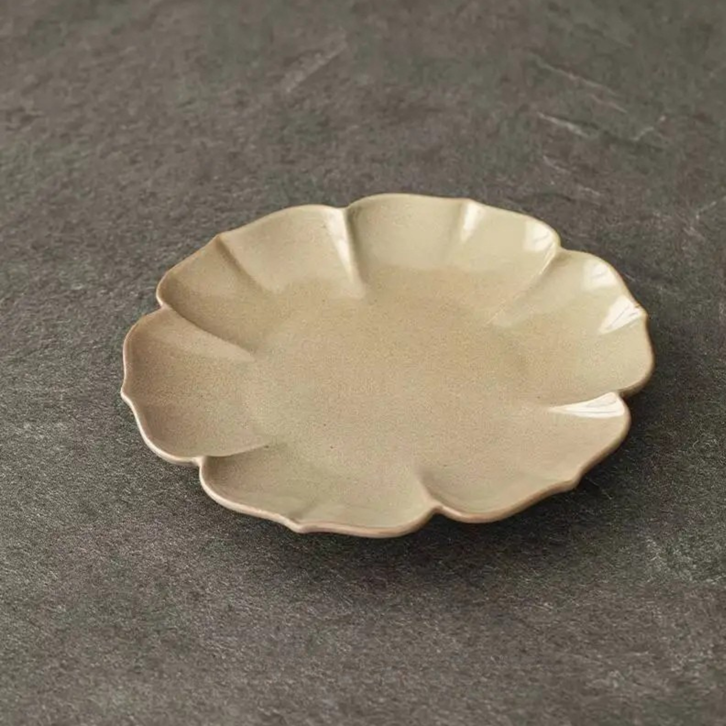  Ivory petal-shaped stoneware dish with satin glaze, side angle view on dark grey background