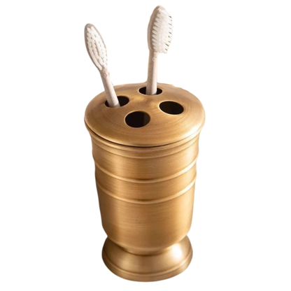 Antique brass toothbrush holder with four slots and ridged cylindrical body, two toothbrushes displayed, brushed warm gold finish, white background
