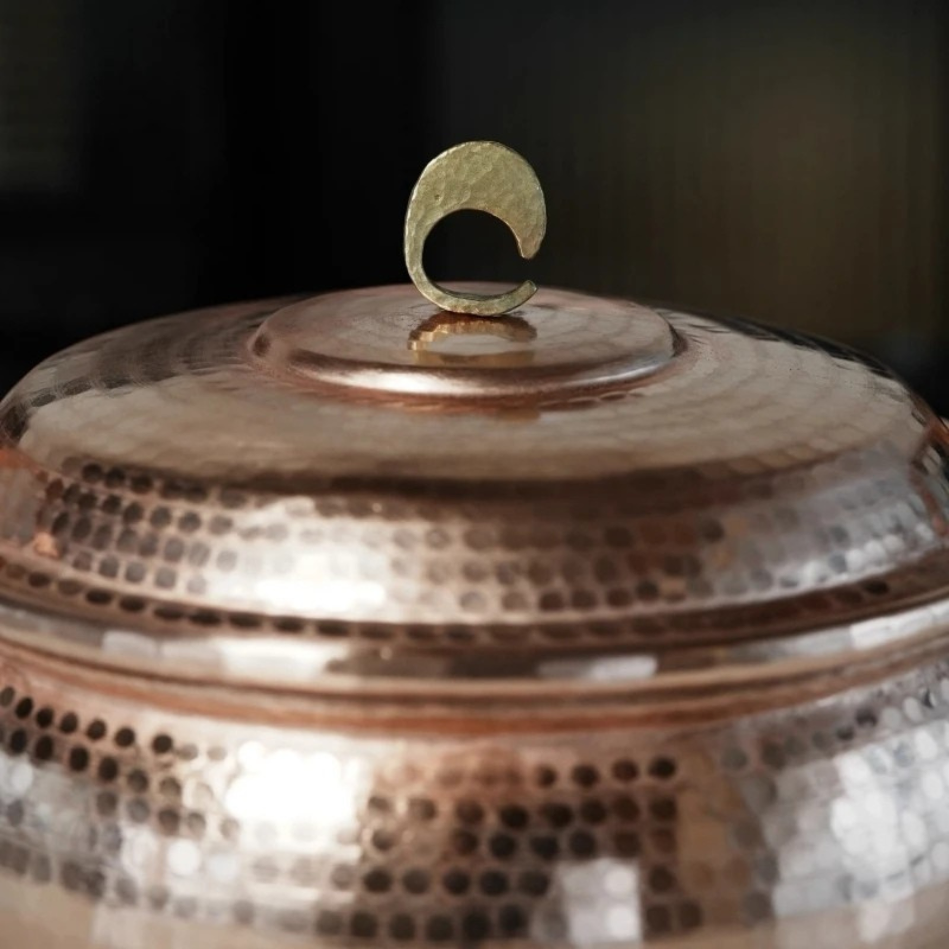 Copper Cauldron close-up detail of the hammered brass crescent moon lid knob against the hand-textured copper lid surface, with warm bokeh background