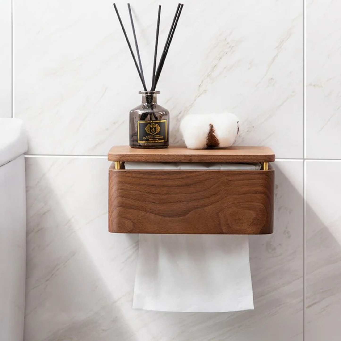 Walnut wood wall-mounted tissue holder on marble tile wall, top shelf with smoky glass reed diffuser and cotton flower, paper roll below — japandi bathroom styling