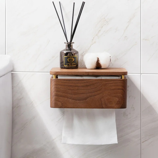Walnut wood wall-mounted tissue holder on marble tile wall, top shelf with smoky glass reed diffuser and cotton flower, paper roll below — japandi bathroom styling