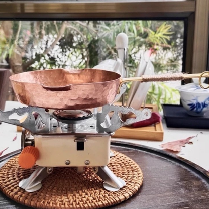 Copper Skillet handmade pure copper frying pan on a portable gas burner over a rattan trivet, styled in a natural kitchen setting with lush greenery in the background