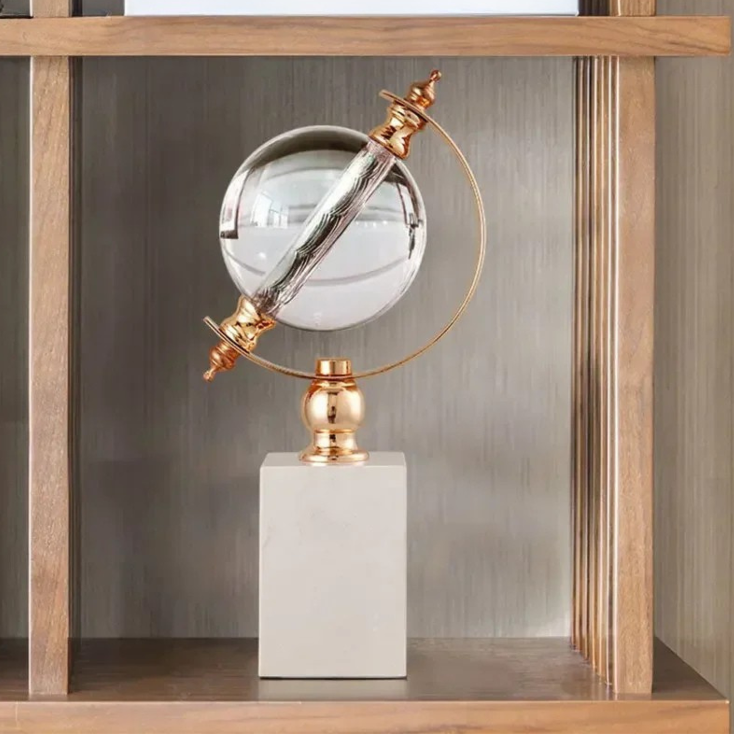 Crystal globe sculpture with gold-plated ring and white marble base, displayed inside a natural wood shelving unit