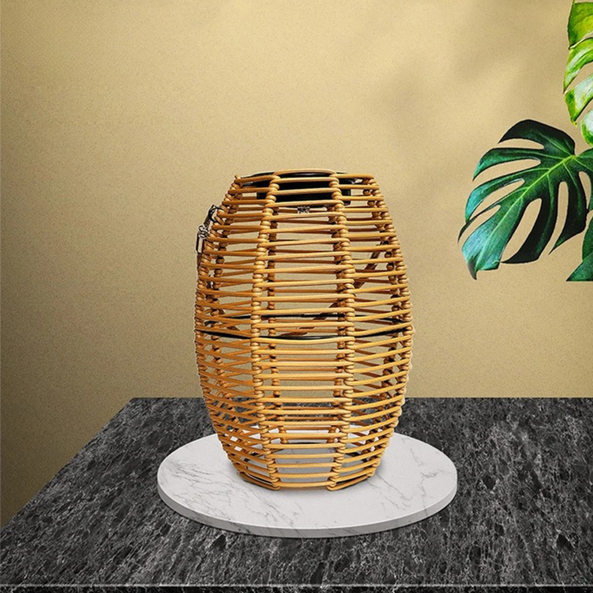 Natural rattan solar lantern displayed on a marble tray on a dark stone surface, styled with a monstera leaf against a warm sand-toned wall