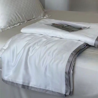  Ivory White eucalyptus lyocell cooling quilt folded on a bed seen from above, with a fashion editorial print as a styling prop, showing the silky-smooth fabric and soft grey satin border trim
